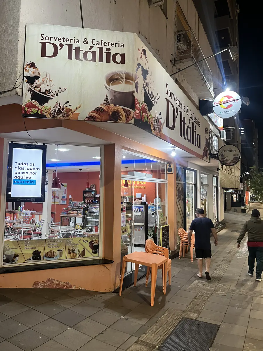 Esquina da D'Italia Sorveteria à noite, com a tela da SmartScreen acesa na vitrine e pessoas passando na calçada